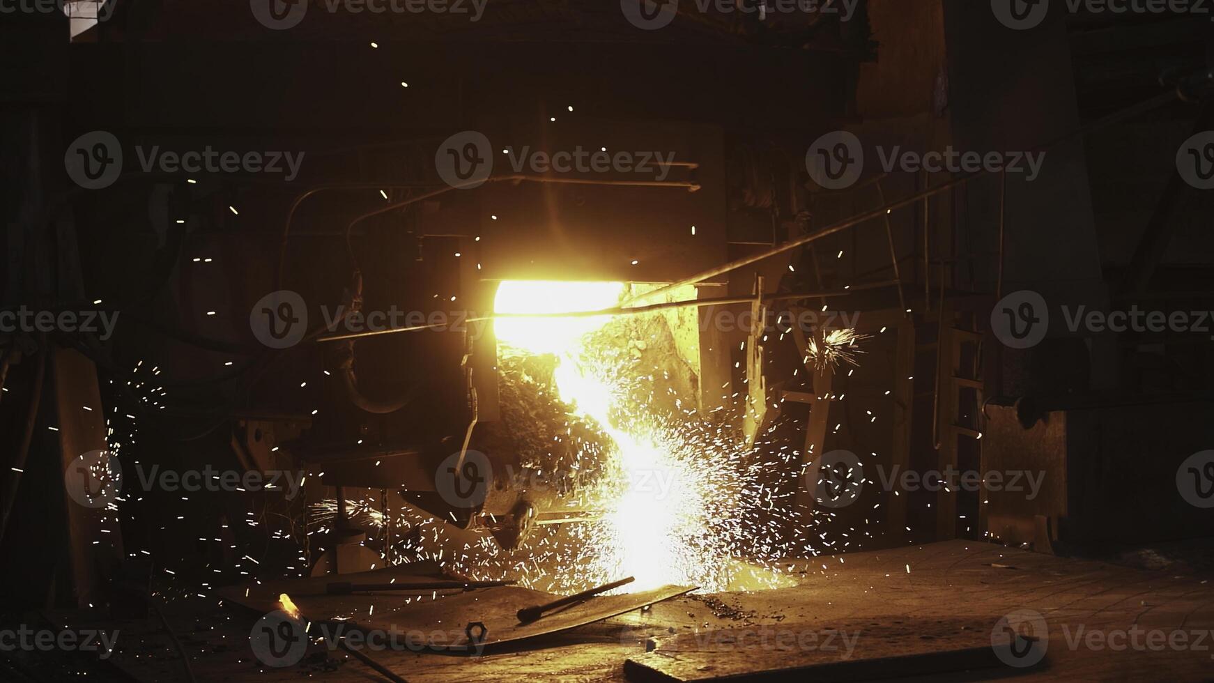 Molten metal is being poured out, producing bright sparks within a vibrant foundry environment. Stock Clip photo
