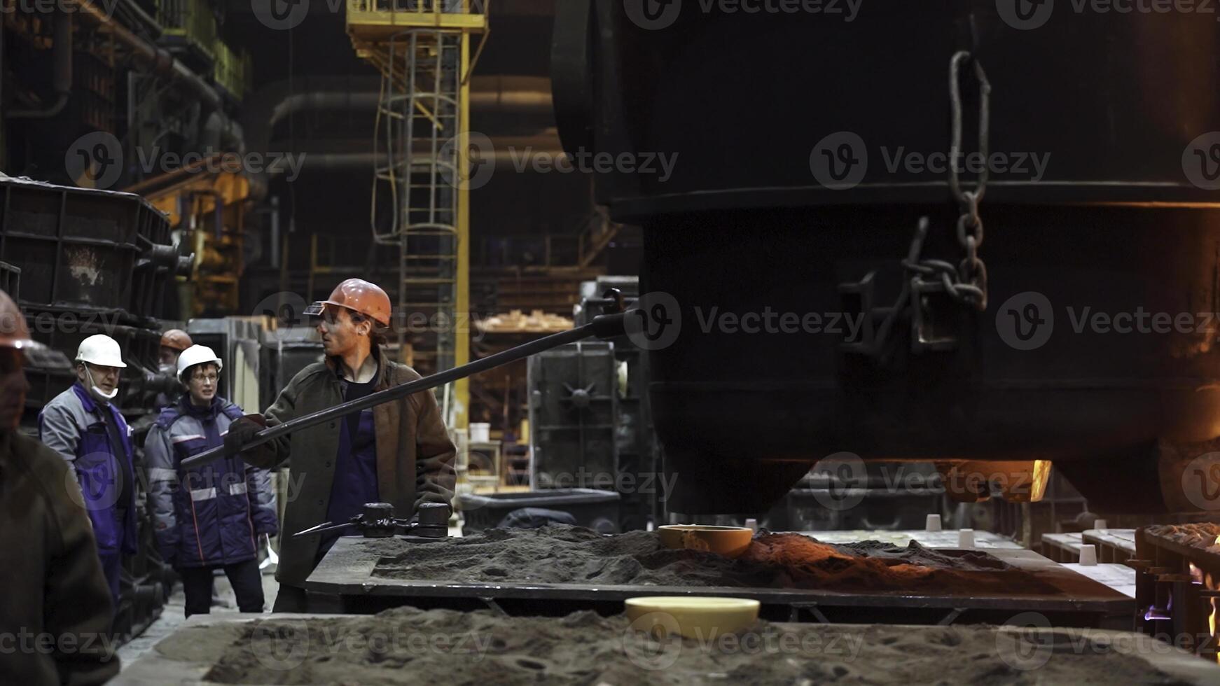 Workers are actively engaged in the metal casting process within a busy manufacturing environment. Stock Clip photo