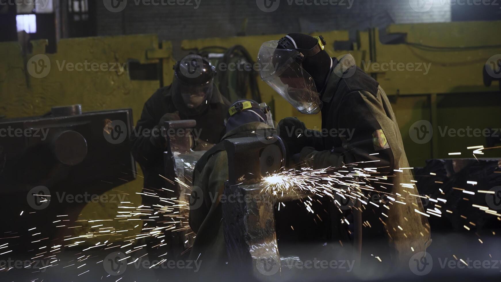 Workers are actively engaged in welding and grinding tasks within an industrial workshop. Stock Clip photo