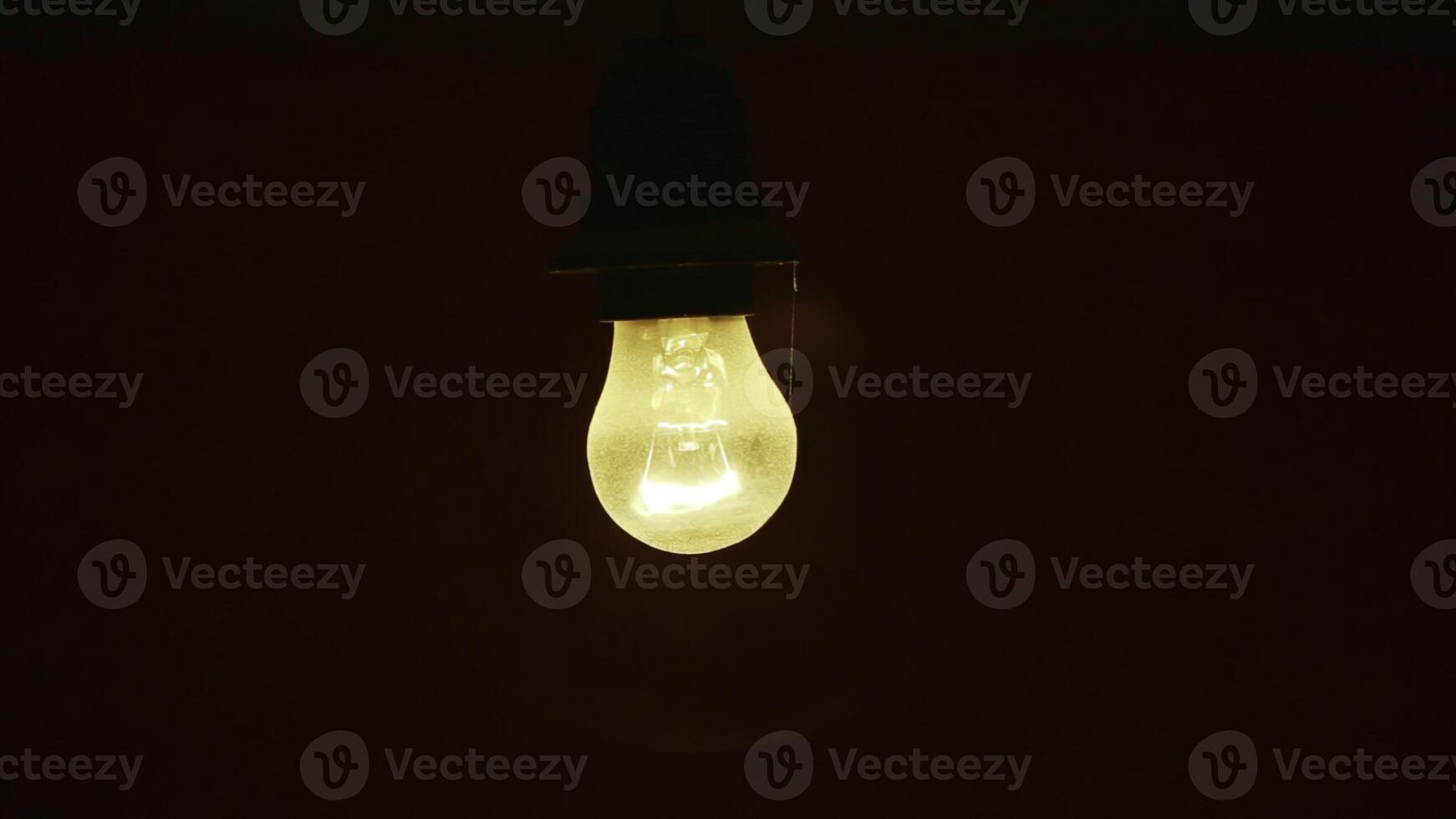 An illuminated light bulb hangs elegantly against a dark background, creating visual contrast. Stock Clip photo