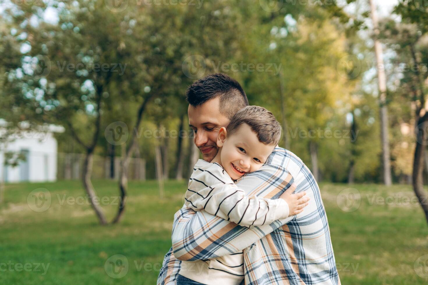 Portrait of positive, smiling father and cute little boy embracing together, in the forest photo