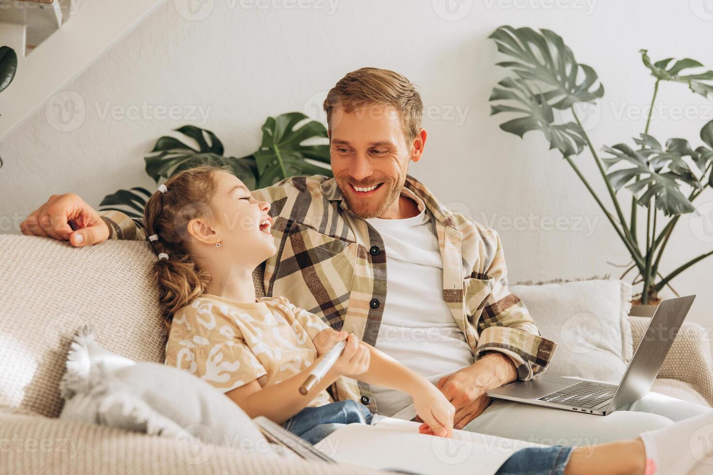 Happy, smiling father and cute little daughter together drawing, sitting on comfortable sofa photo