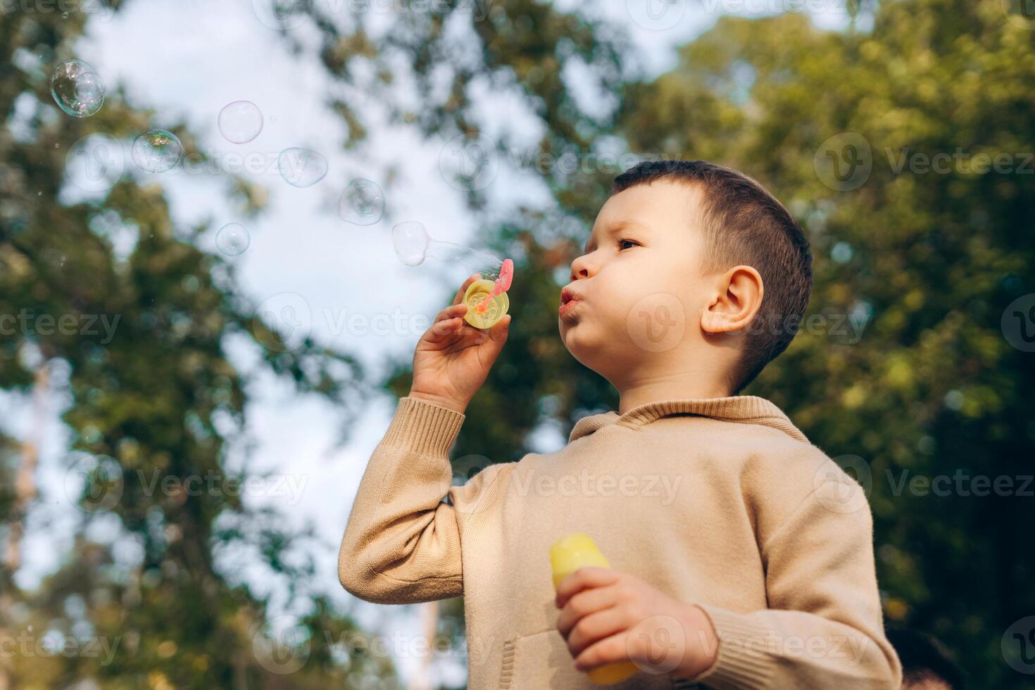 Little boy blowing soap bubbles on the street, in forest, looking away, copy space. Fun concept photo