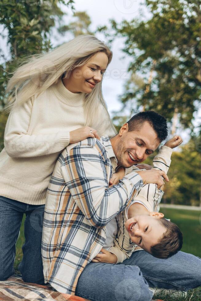 Smiling, happy family, beautiful mother, father and little son embracing together sitting on blanket photo