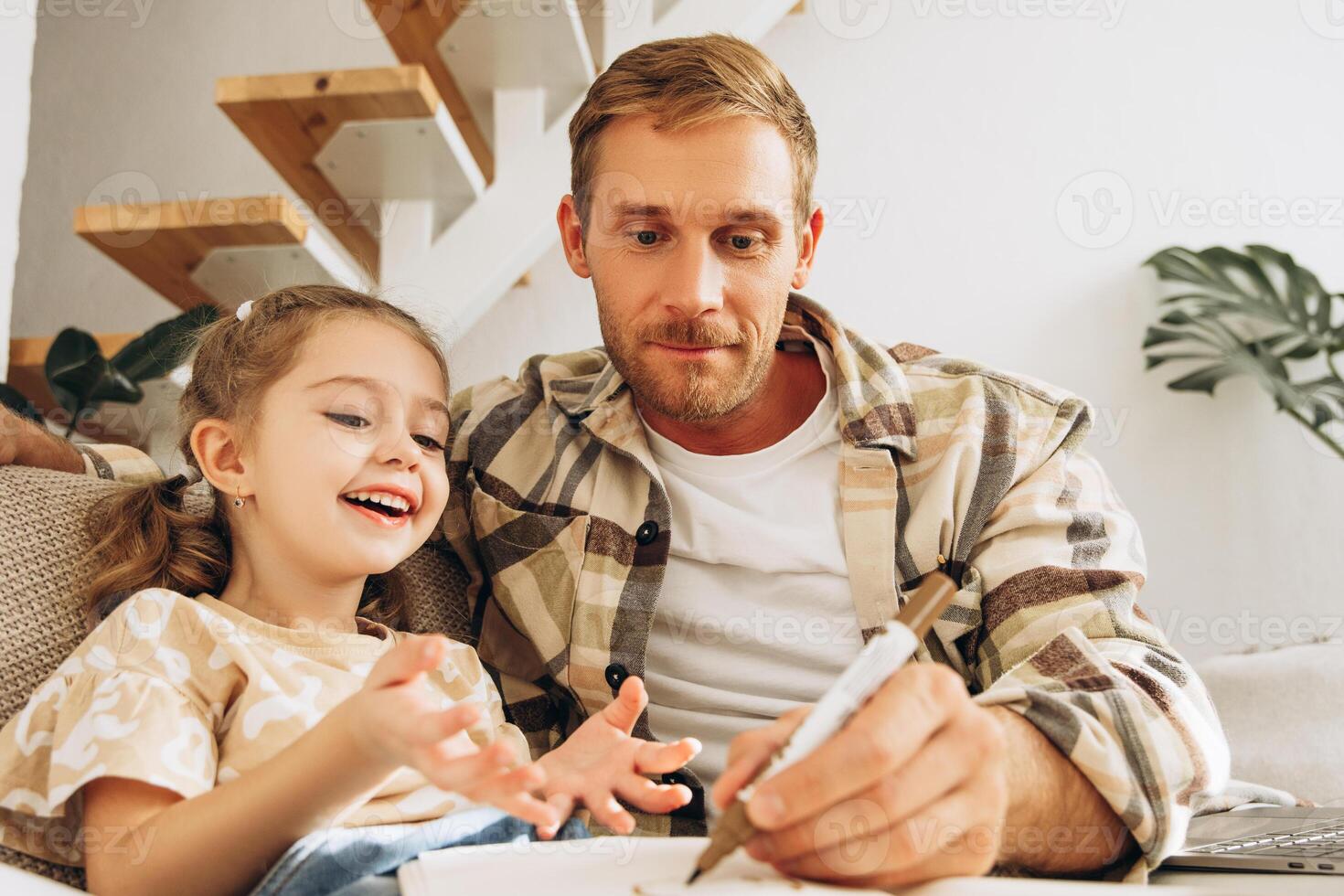 Handsome father and cute little daughter drawing, sitting on comfortable sofa at home in living room photo