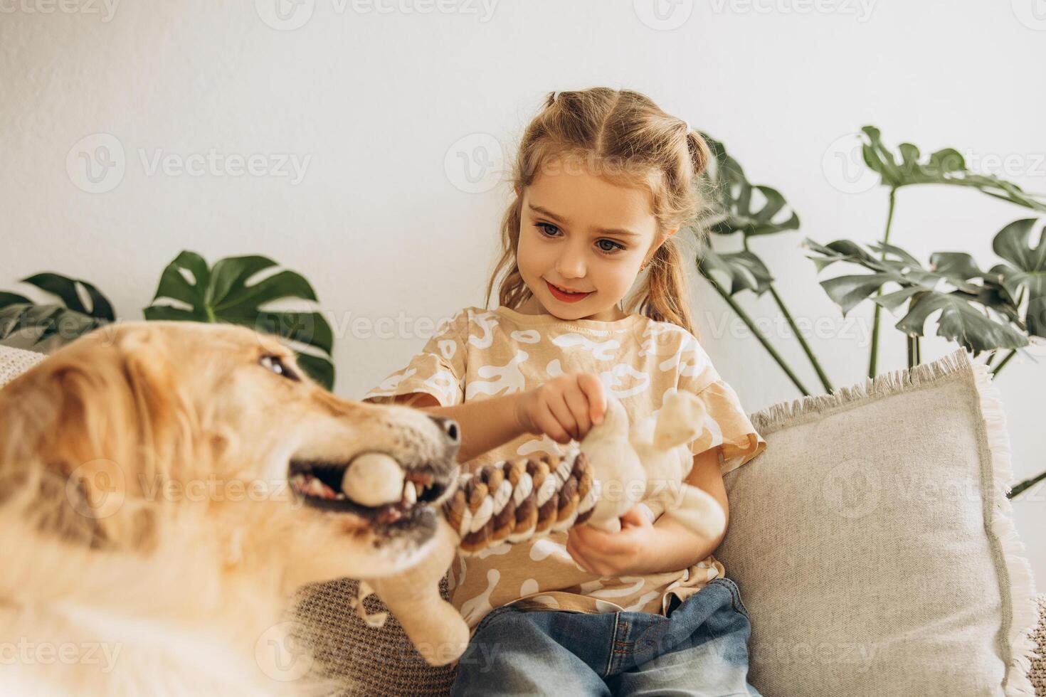 Happy, beautiful cute little girl playing with golden retriever, sitting on comfortable sofa photo