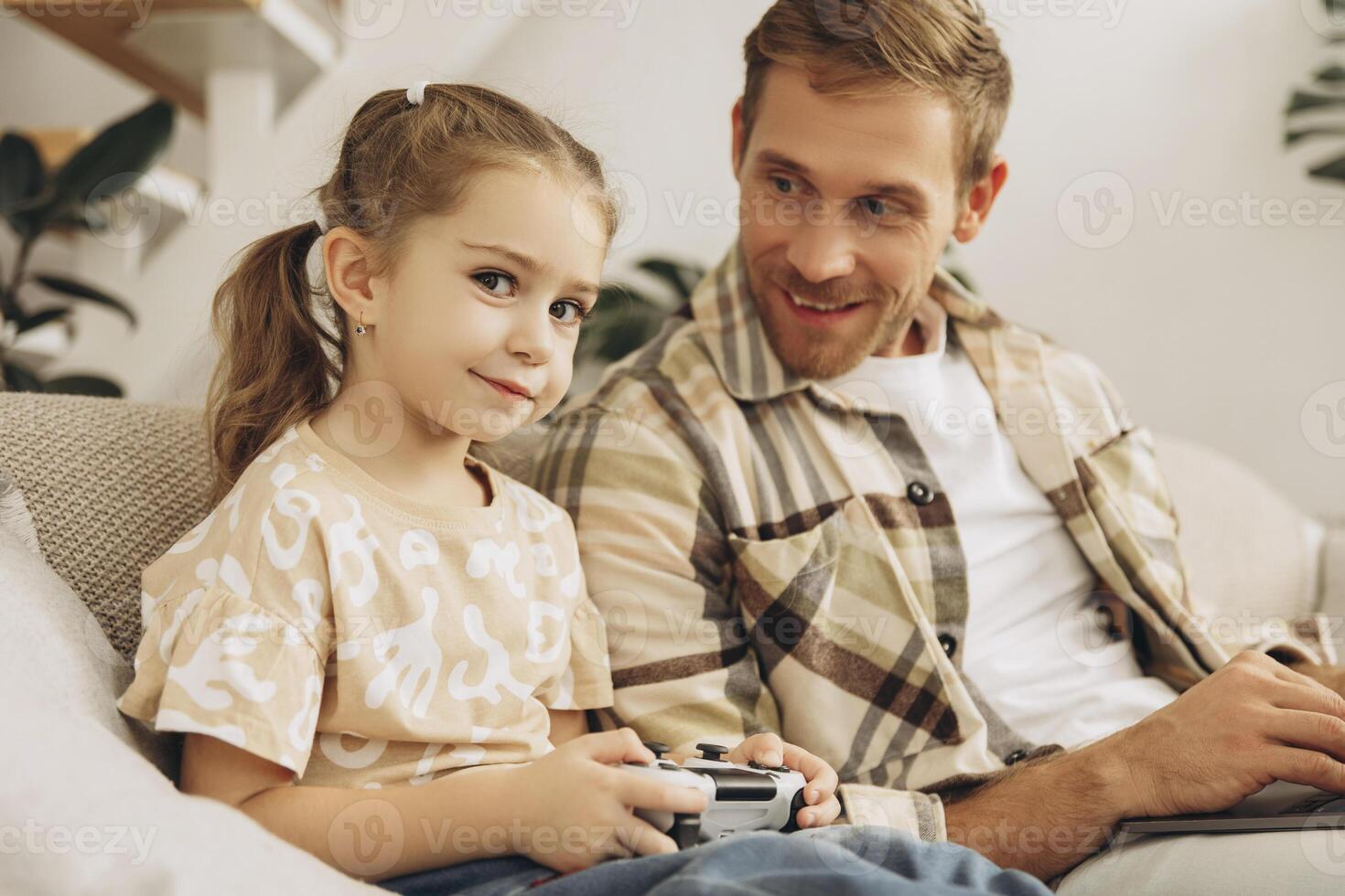 Portrait of smiling, handsome man and his little daughter playing games, holding joystick photo