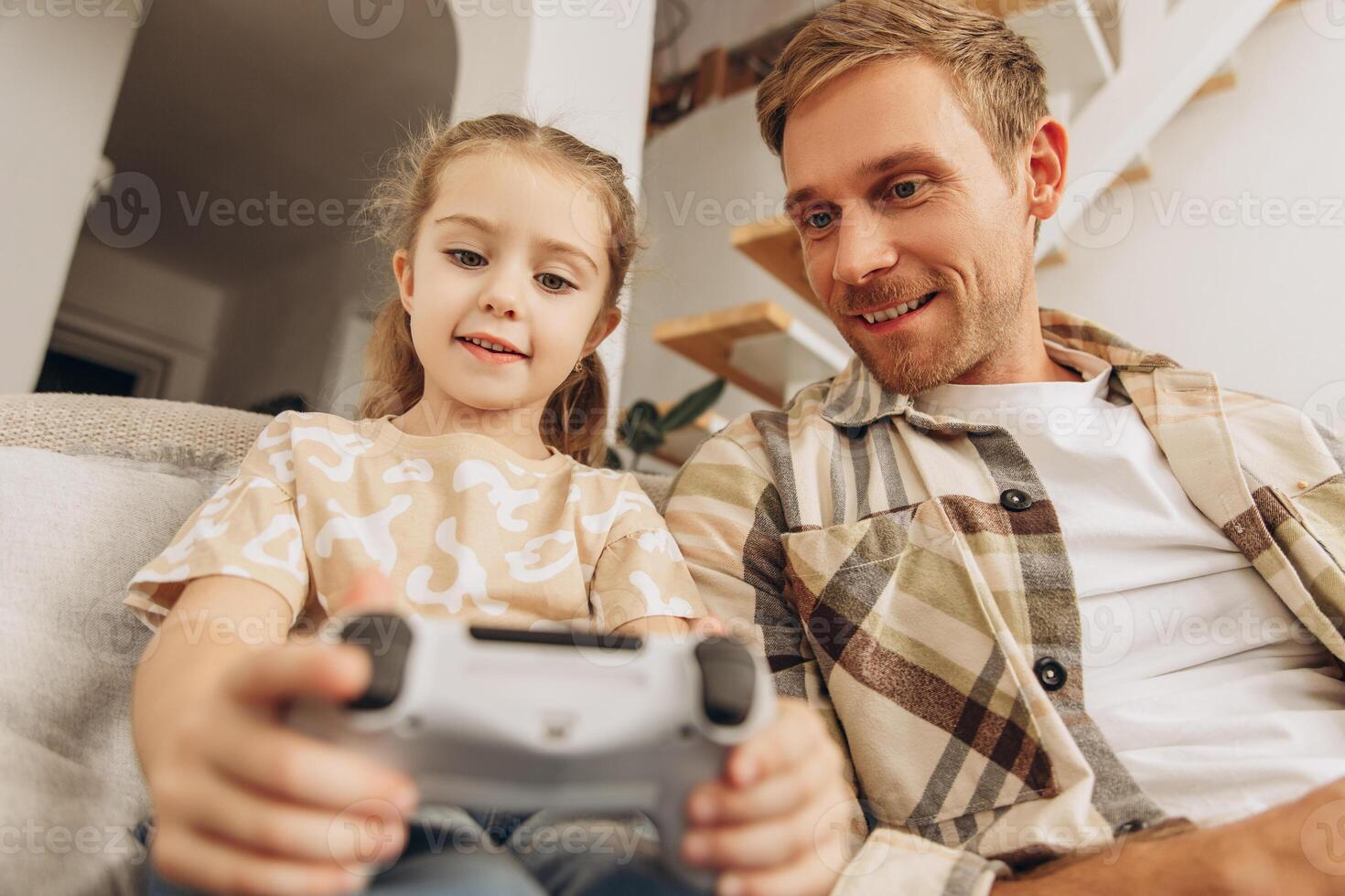 Portrait of happy, attractive man and his little daughter playing games, holding joystick photo