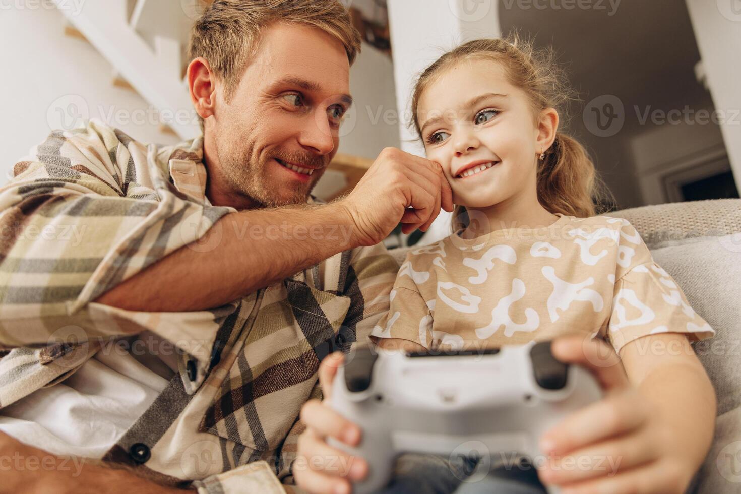 Smiling, excited man, little daughter and father playing together game, holding console photo