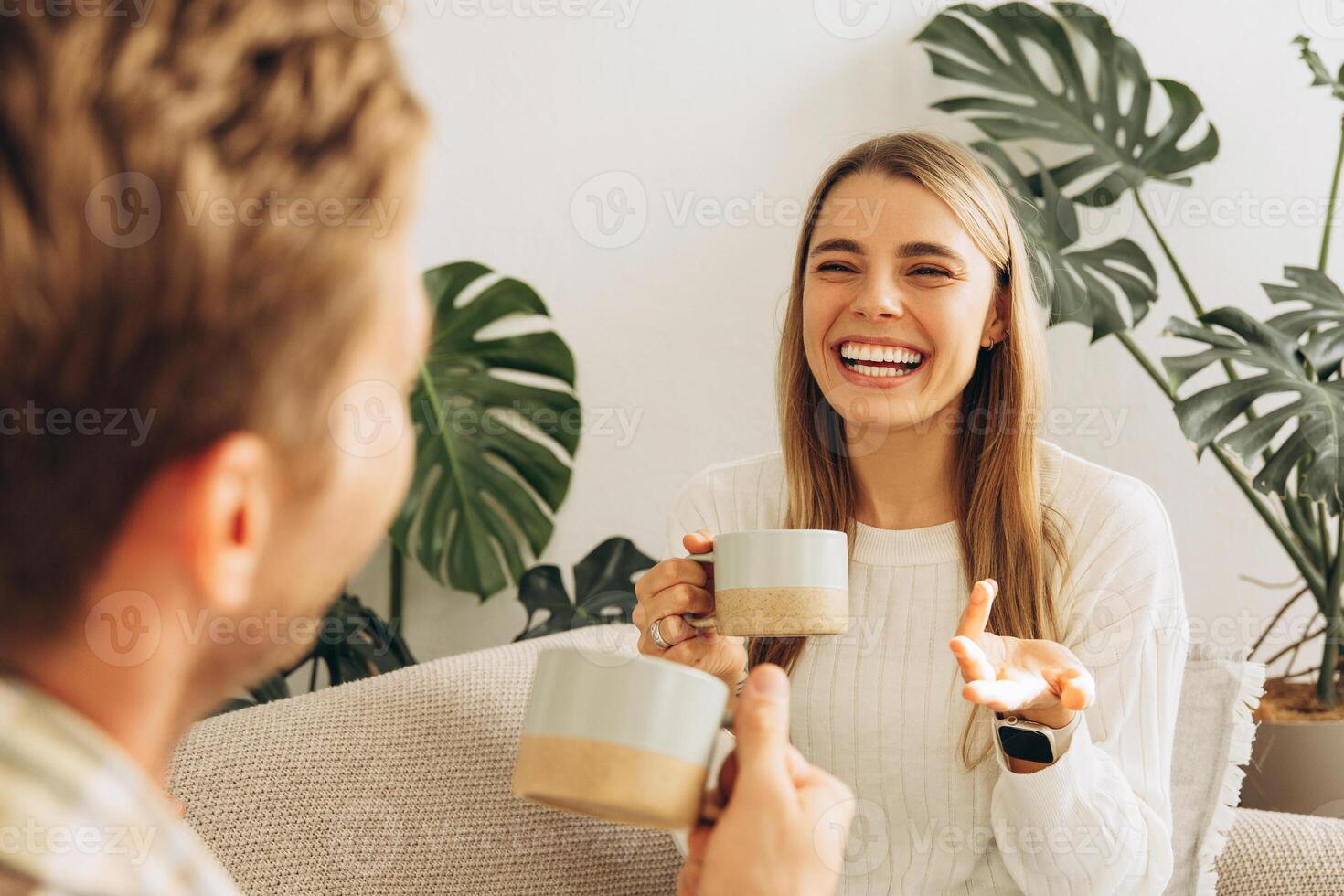 Beautiful couple holding cup with coffee, sitting on comfortable sofa, talking each other at home photo