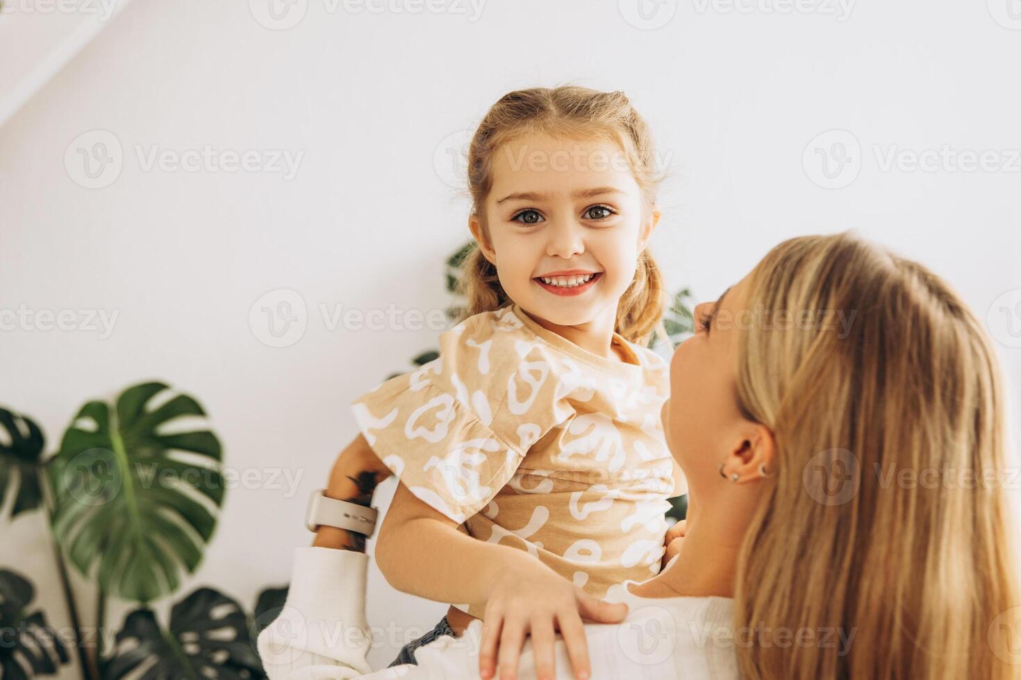 Smiling, happy, beautiful woman, mother holding little daughter, standing in living room at home photo