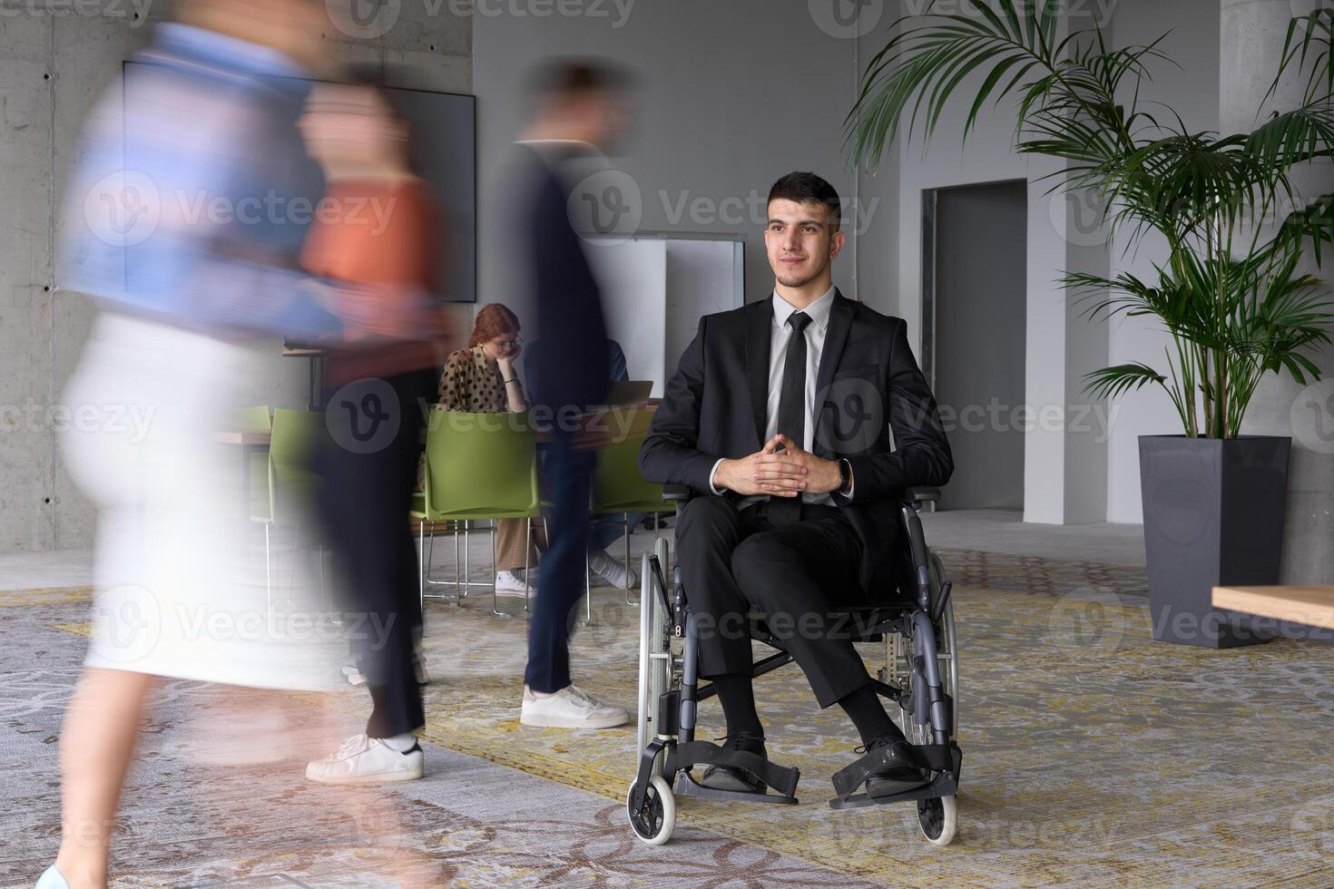A businessman in a wheelchair navigating through a busy office, surrounded by his colleagues who are actively engaged in their work and collaboration photo