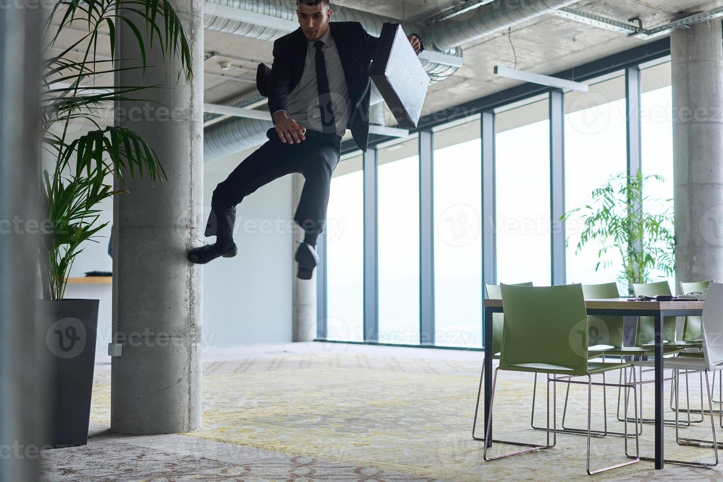 A businessman ecstatically jumping in a modern office, holding a briefcase in his hands, celebrating a moment of success and triumph. photo