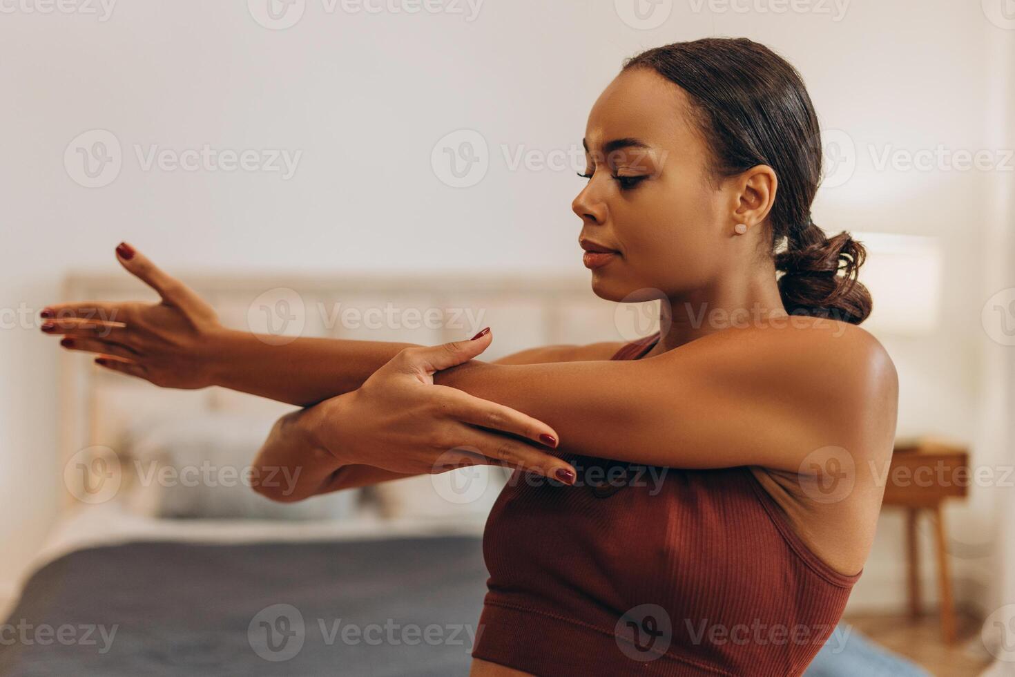 Smiling young African American woman stretching her hand before training while standing at home photo