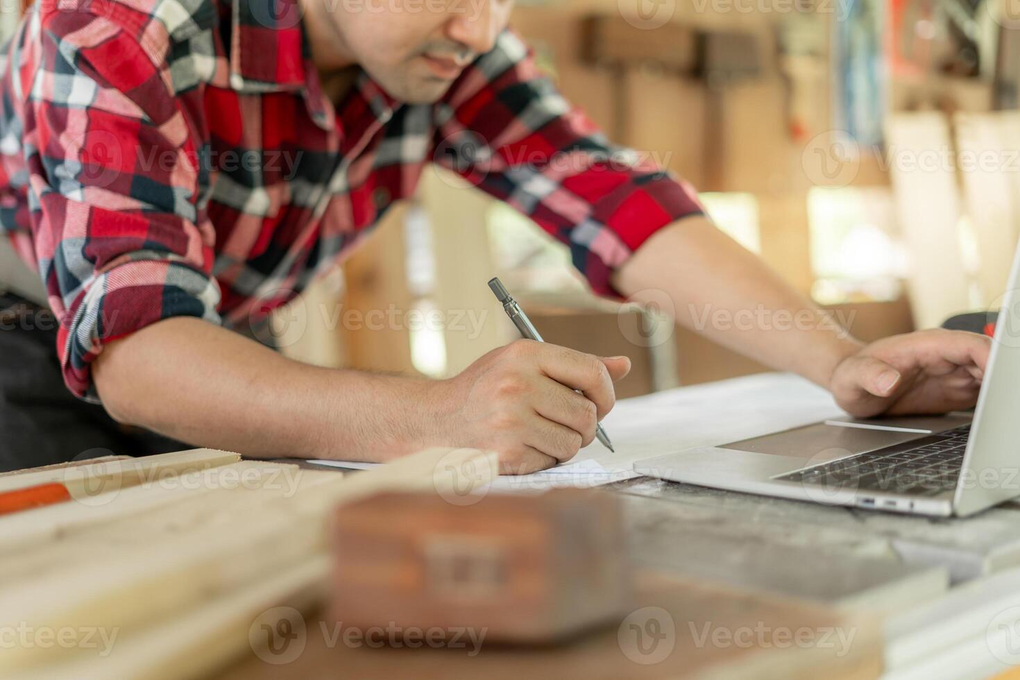 Asian man owner a small furniture business is recheck order online. carpenter male is adjust wood to the desired size. architect, designer, Built-in, professional wood, craftsman, workshop. photo