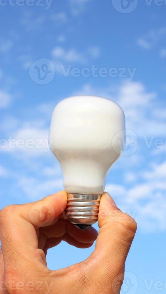 A person holding a light bulb in front of a blue sky photo