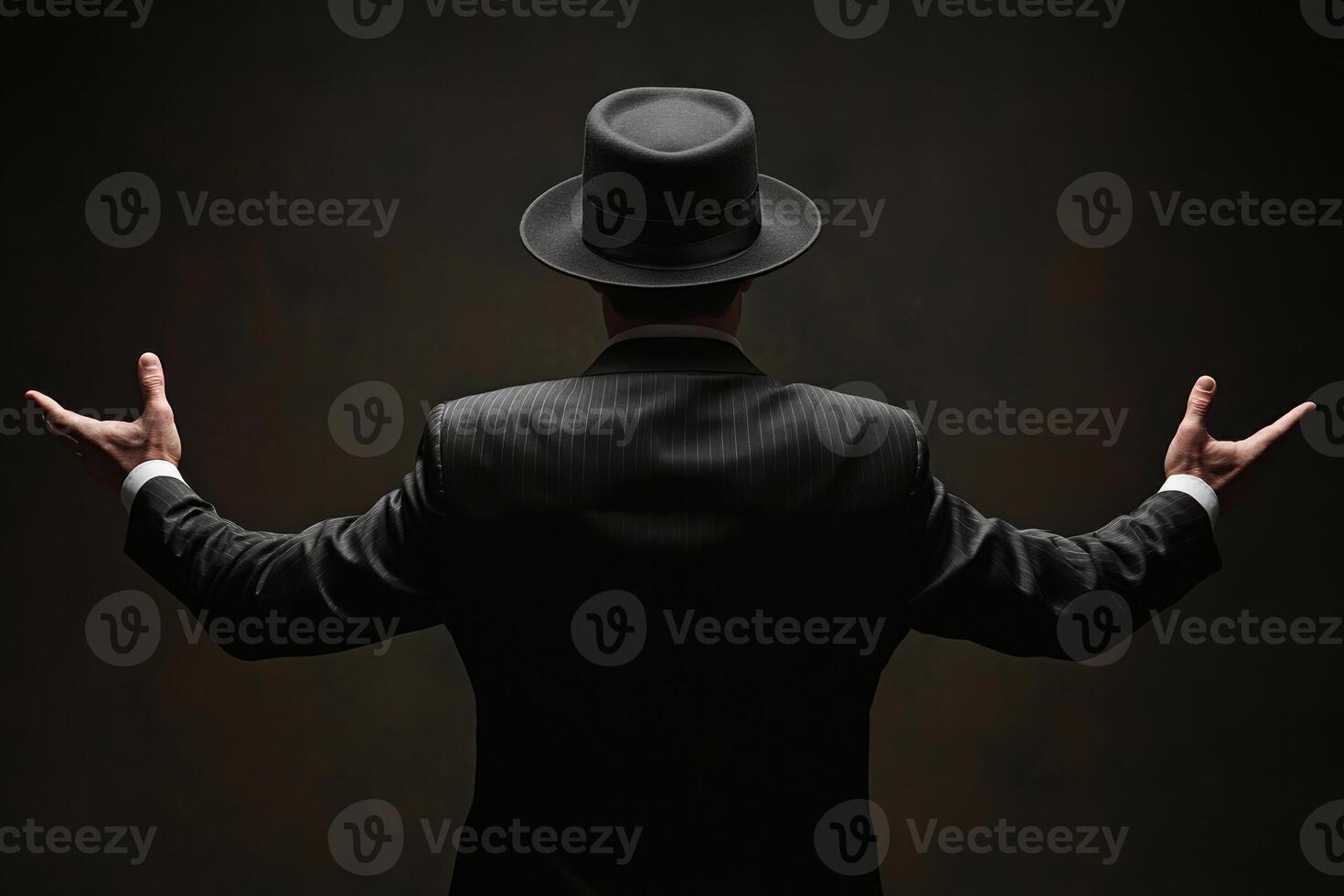 A man in a suit and hat standing confidently, arms outstretched against a dark background. photo