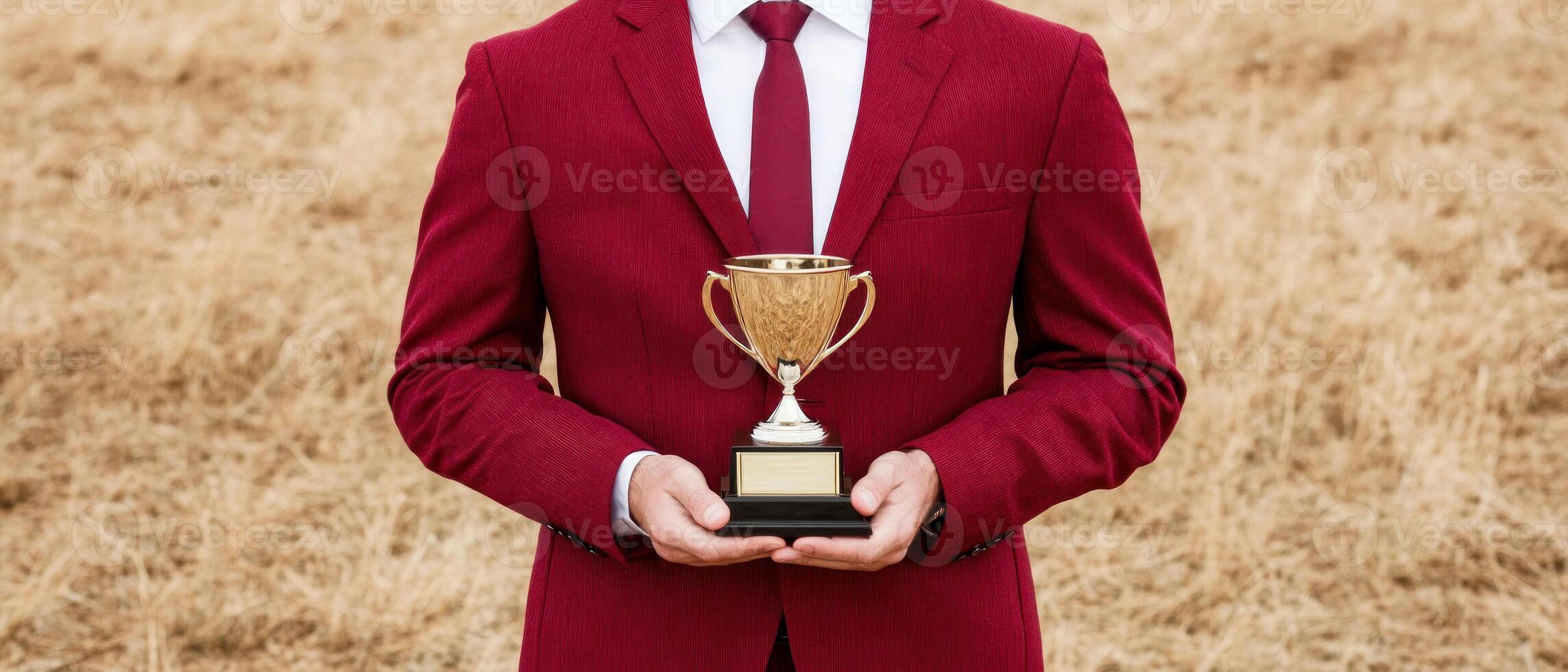 A man in a red suit holding a trophy against a natural background of dry grass. photo