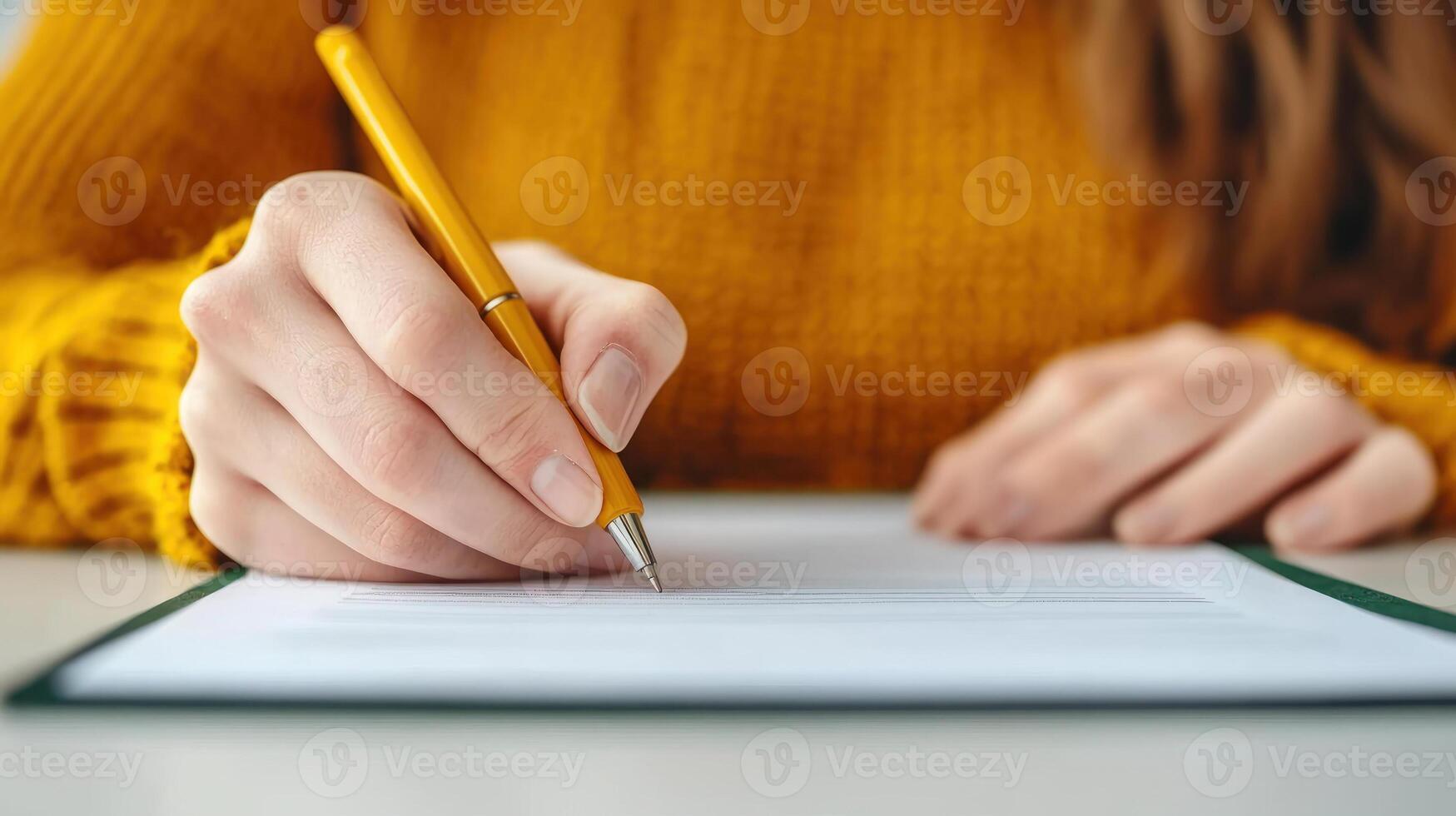 A person writing with a pen on a document while wearing a cozy yellow sweater. photo