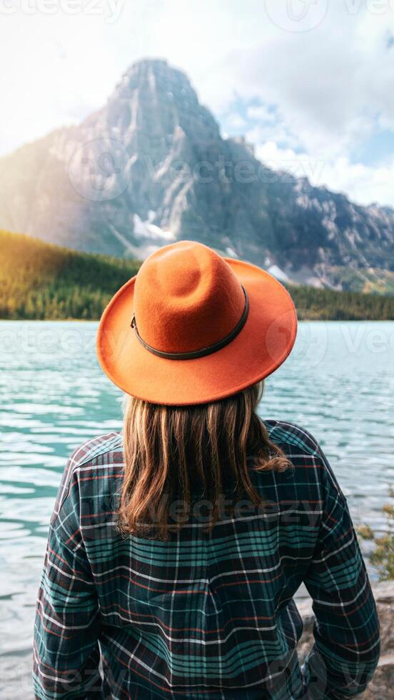 A woman wearing a hat and plaid shirt looking at a lake photo