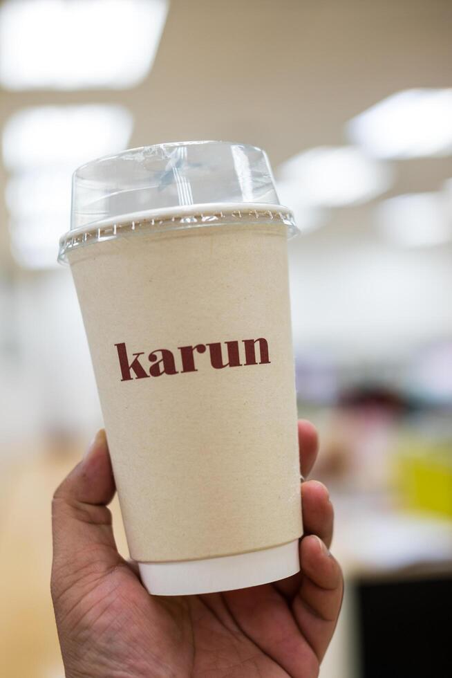 Bangkok, Thailand - December 1, 2024 Hand holding a paper cup of iced royal Thai tea of Karun. A classic Thai tea gelato Karun house photo