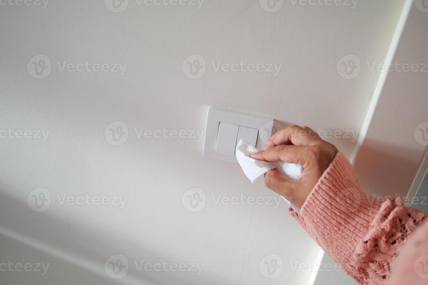 hand with cloth wiping a light switch at the wall photo