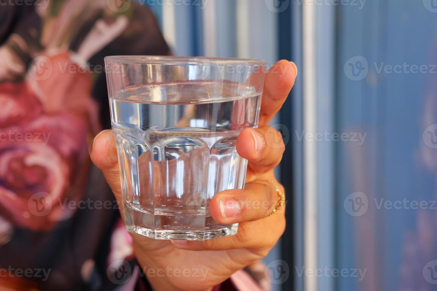 A Hand Holding a Clear Glass of Fresh Water Set in a Beautiful and Colorful Atmosphere photo