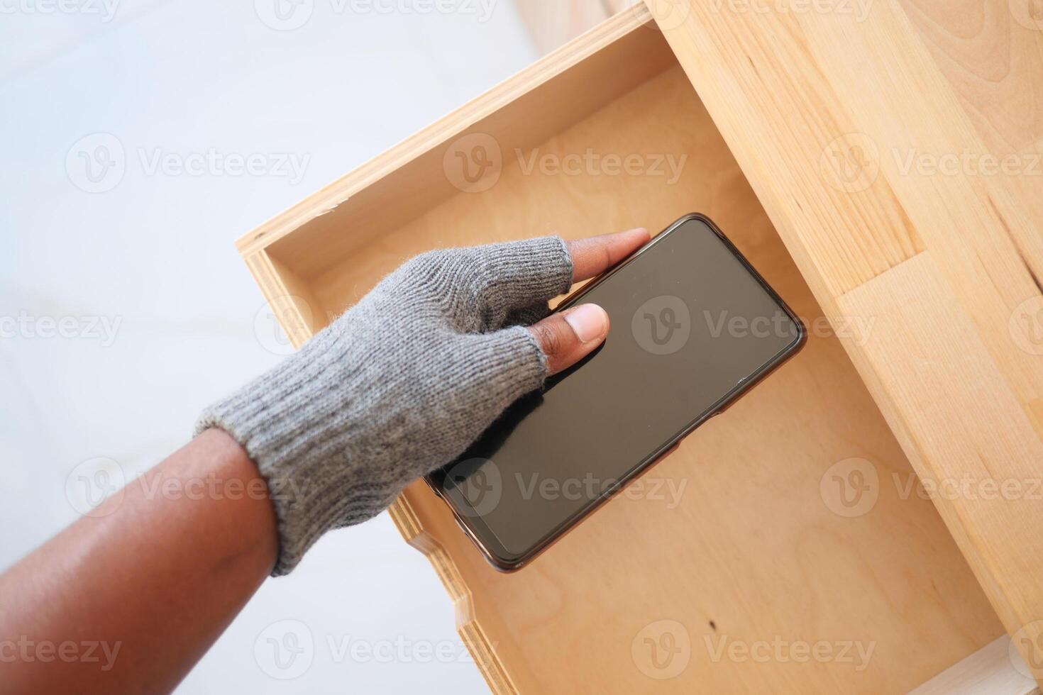 Person Stealing Smartphone from an Open Wooden Drawer photo