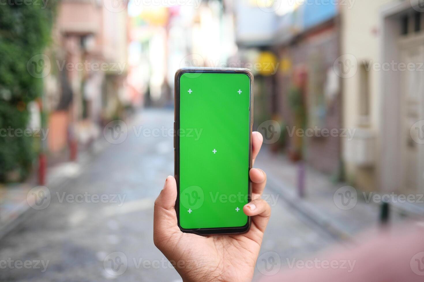 A Hand Firmly Holding a Smartphone with a Green Screen Display in a Vibrant Urban Alley photo