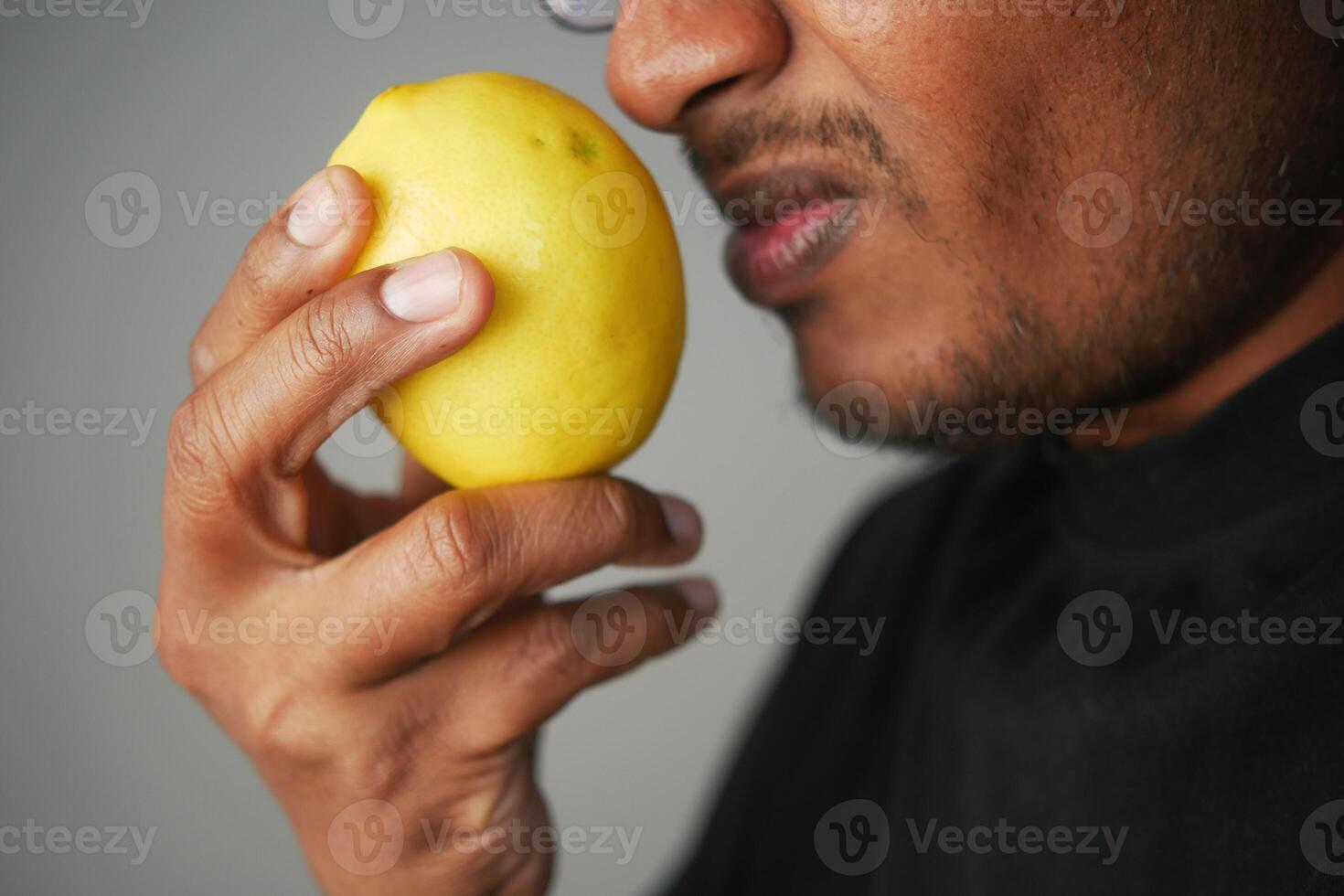 A Man Holding a Bright Yellow Lemon Close to His Face, Engaging with Its Aromatic Essence photo