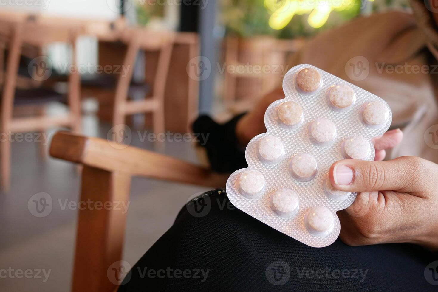 A CloseUp View of a Hand Gripping a Blister Pack of Capsules Within a Cozy Cafe Setting photo