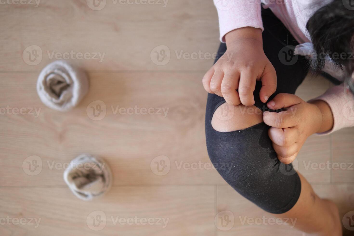 A child is adjusting their knee pad while soft slippers can be seen nearby on the floor photo