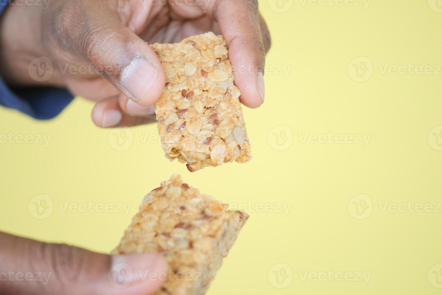 A hand is holding a crunchy granola bar that is breaking apart into smaller pieces photo