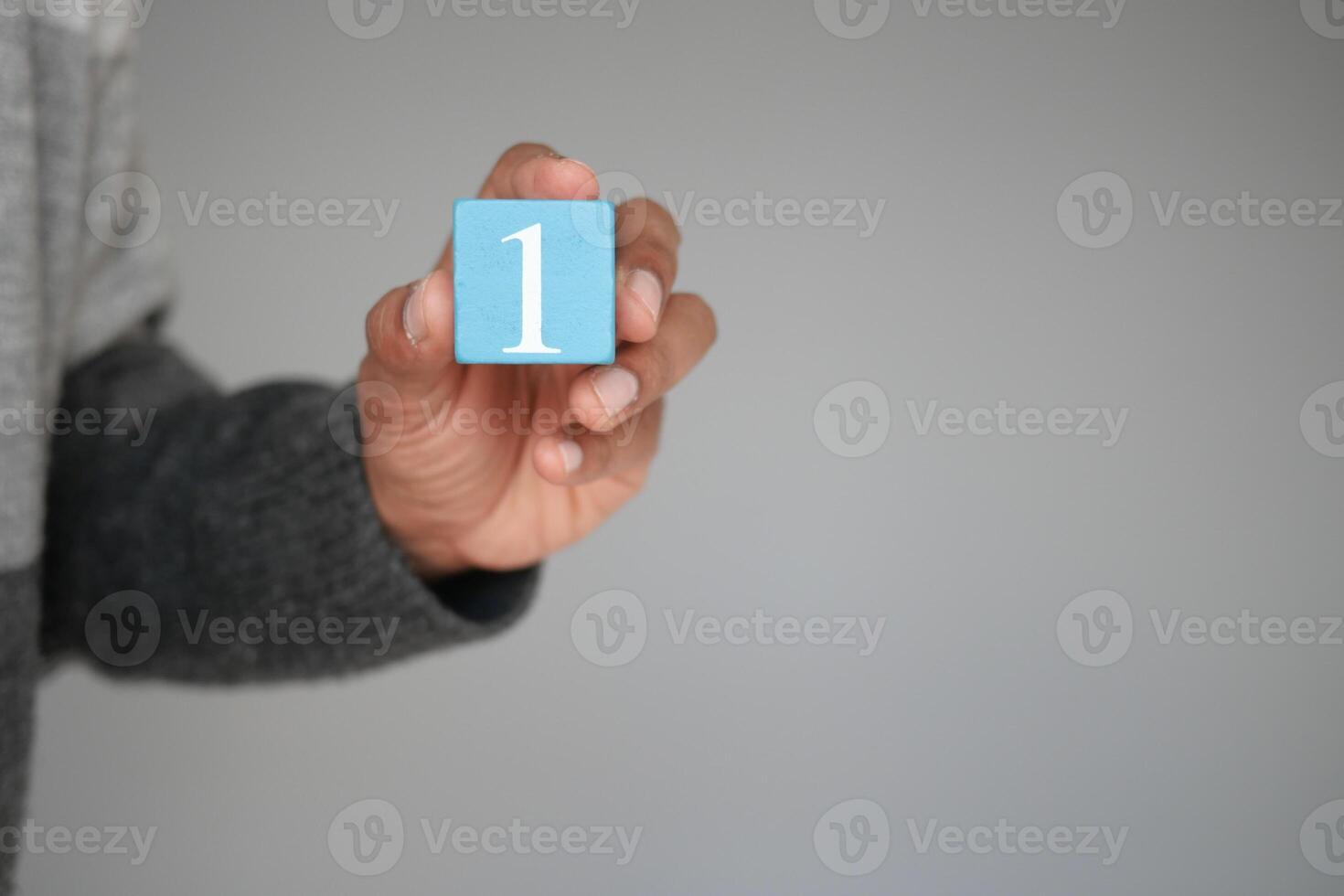 A hand is holding a blue block that has the number one inscribed on it against a neutral background photo