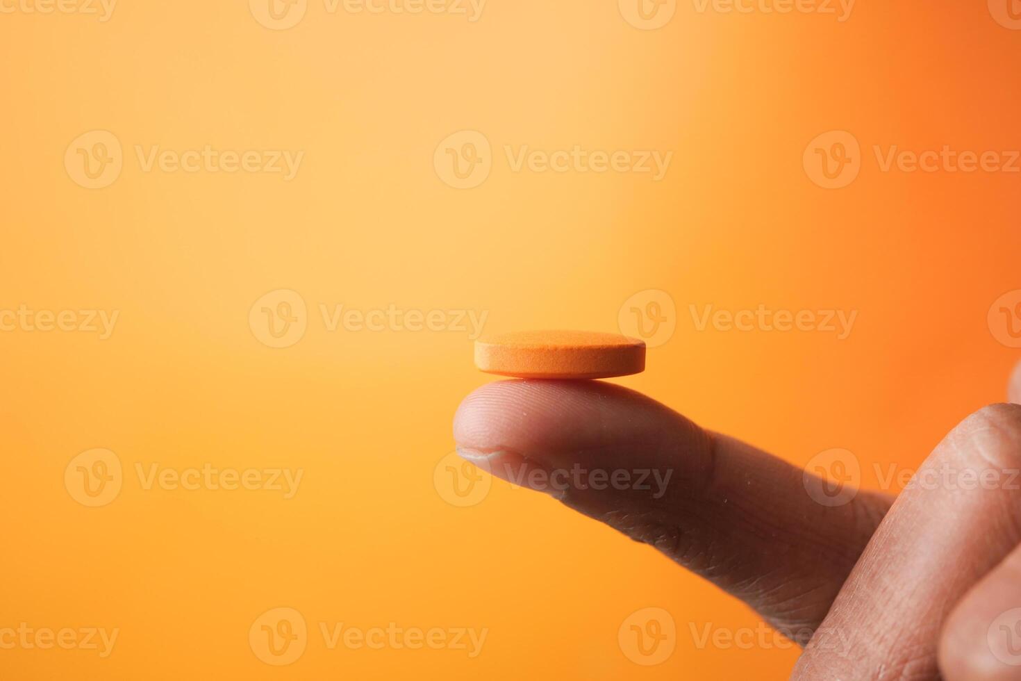 Finger Balancing a Bright Orange Pill Against a Bright and Vibrant Orange Background photo