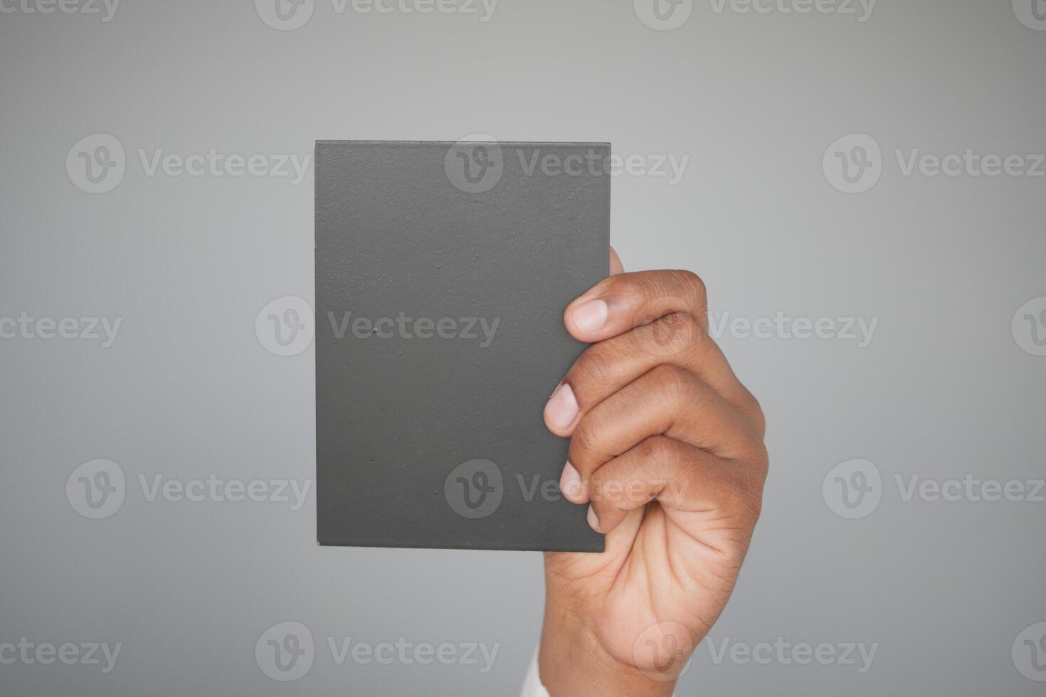 A person is holding a black book in front of a gray background, showcasing a creative concept photo
