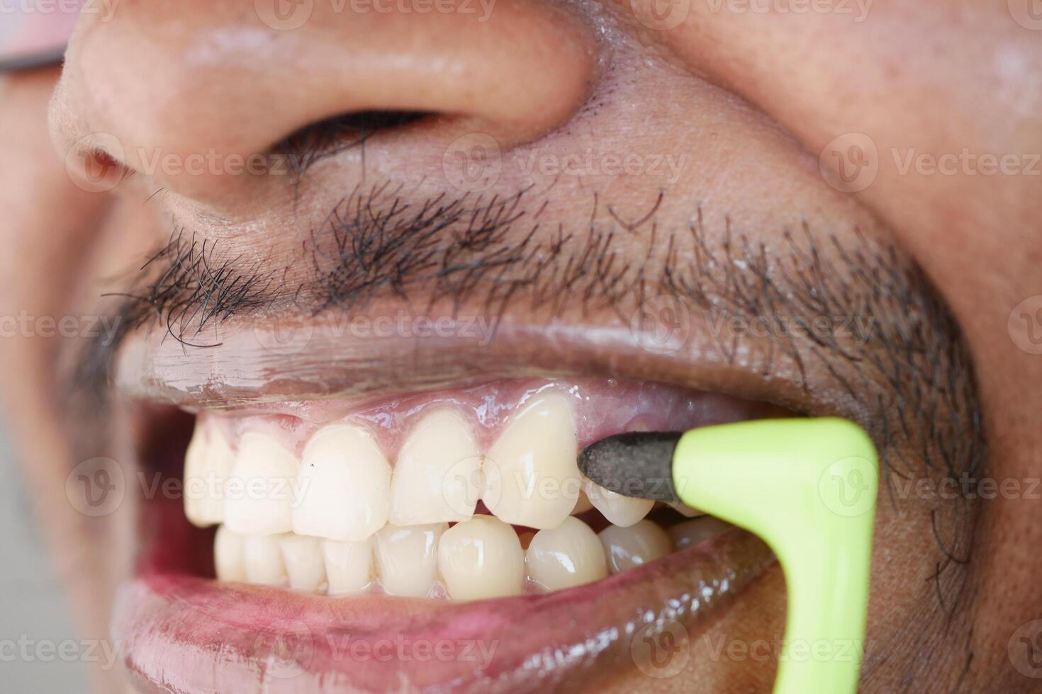 A CloseUp Image of a Man Brushing His Teeth Using a Green Dental Tool for Oral Care photo