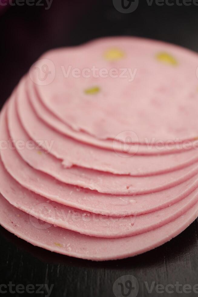 Slices of Pink Bologna Featuring Green Specks Presented Against a Dark Background photo