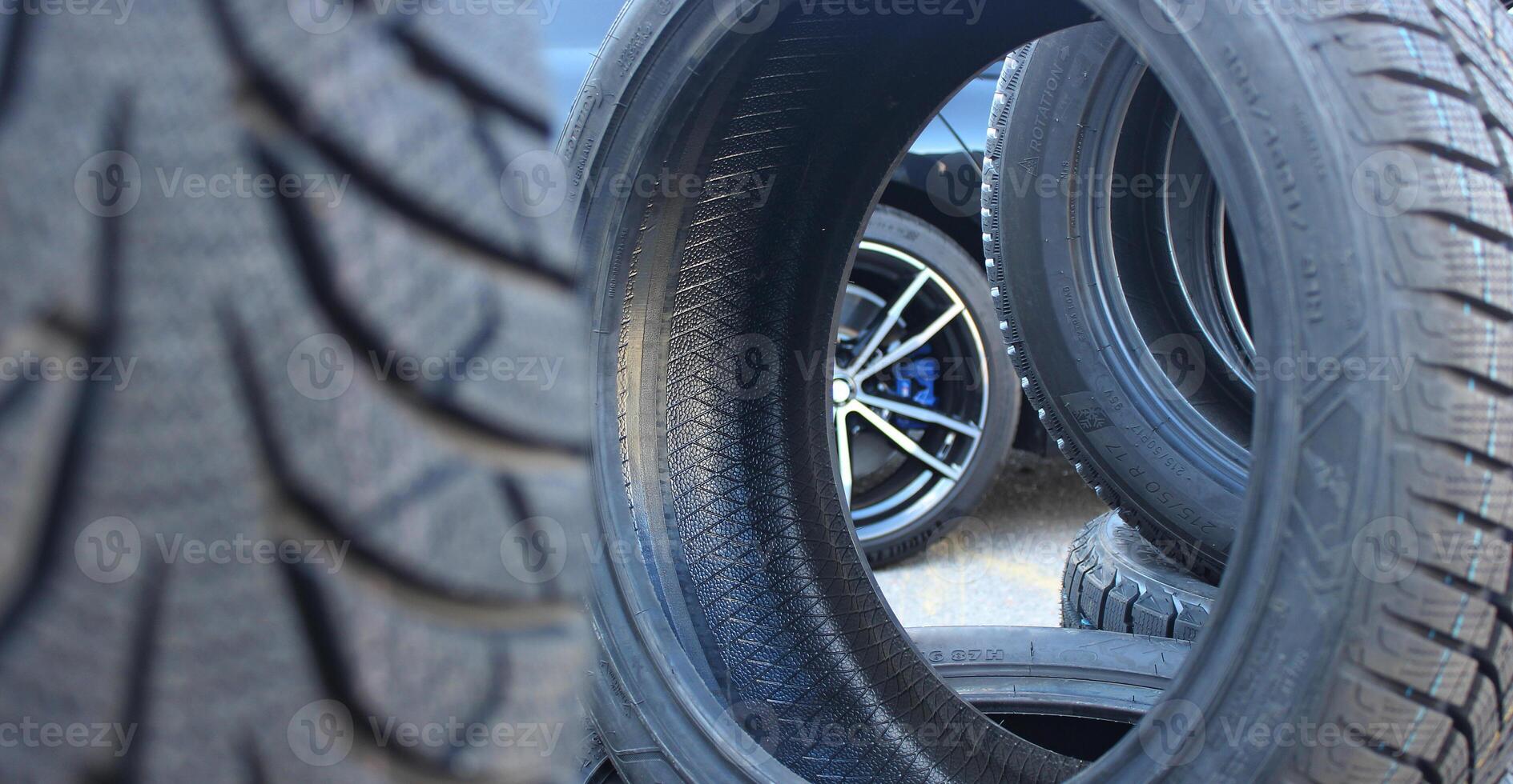 Car is visible through the new tires staying on the edge. Stacked tires set ready to be mounting on a car photo