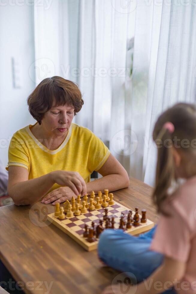 A happy granddaughter plays chess with grandmother at the table,creating precious memories together photo