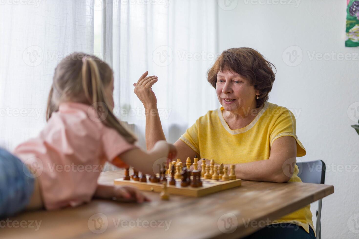happy little girl plays chess with her grandmother at the table, sharing a joyful, bonding moment photo