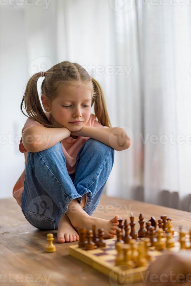 5-year-old girl plays with a mini chess set, focusing intently as she carefully plans her next move. photo