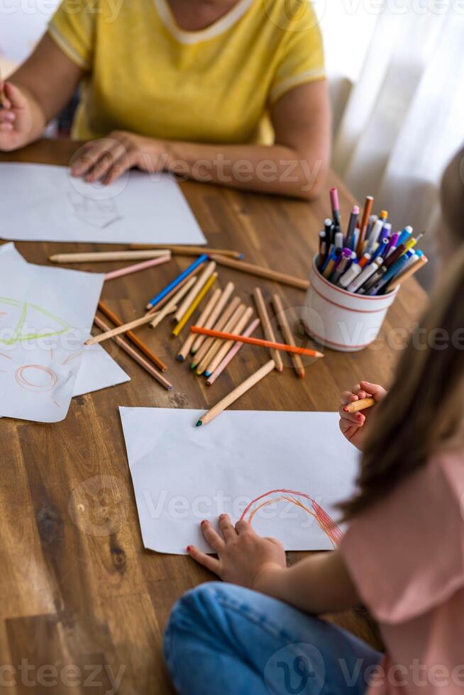 Top view of a charming girl and her grandmother happily drawing in an album with colorful pens photo
