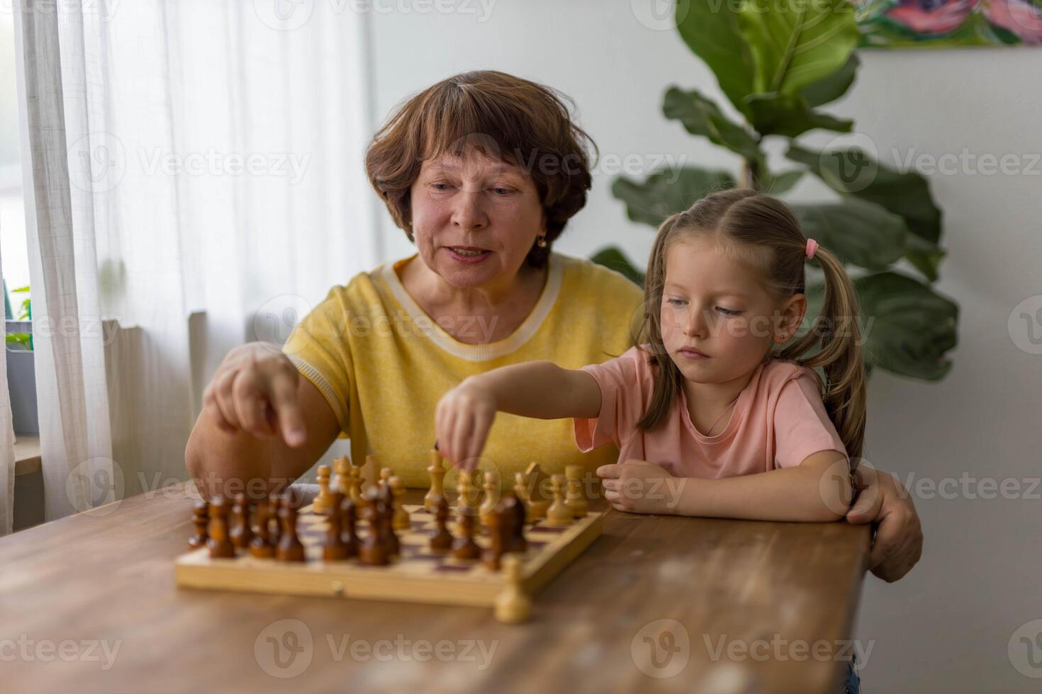 Smiling little girl plays chess with her grandmother at the table,enjoying loving and playful moment photo