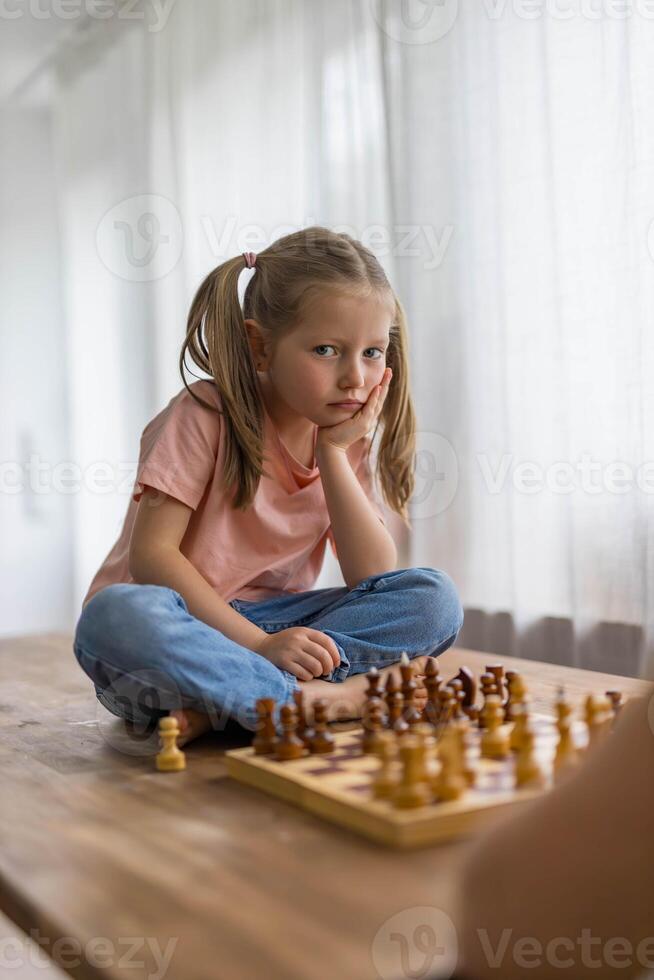 5-year-old girl plays with a mini chess set, focusing intently as she carefully plans her next move. photo