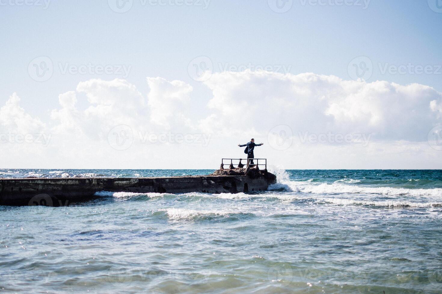 a portrait of a young man on a pier, waves splashing and crashing against the pier photo
