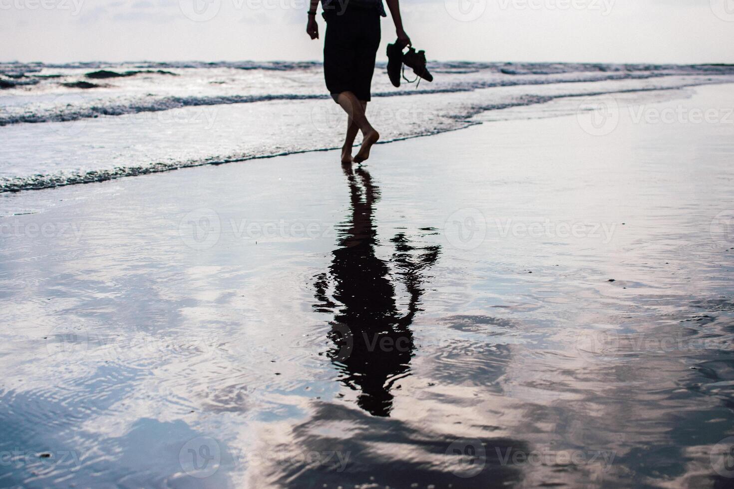 a man walks along the beach, reflection in the wet sand photo