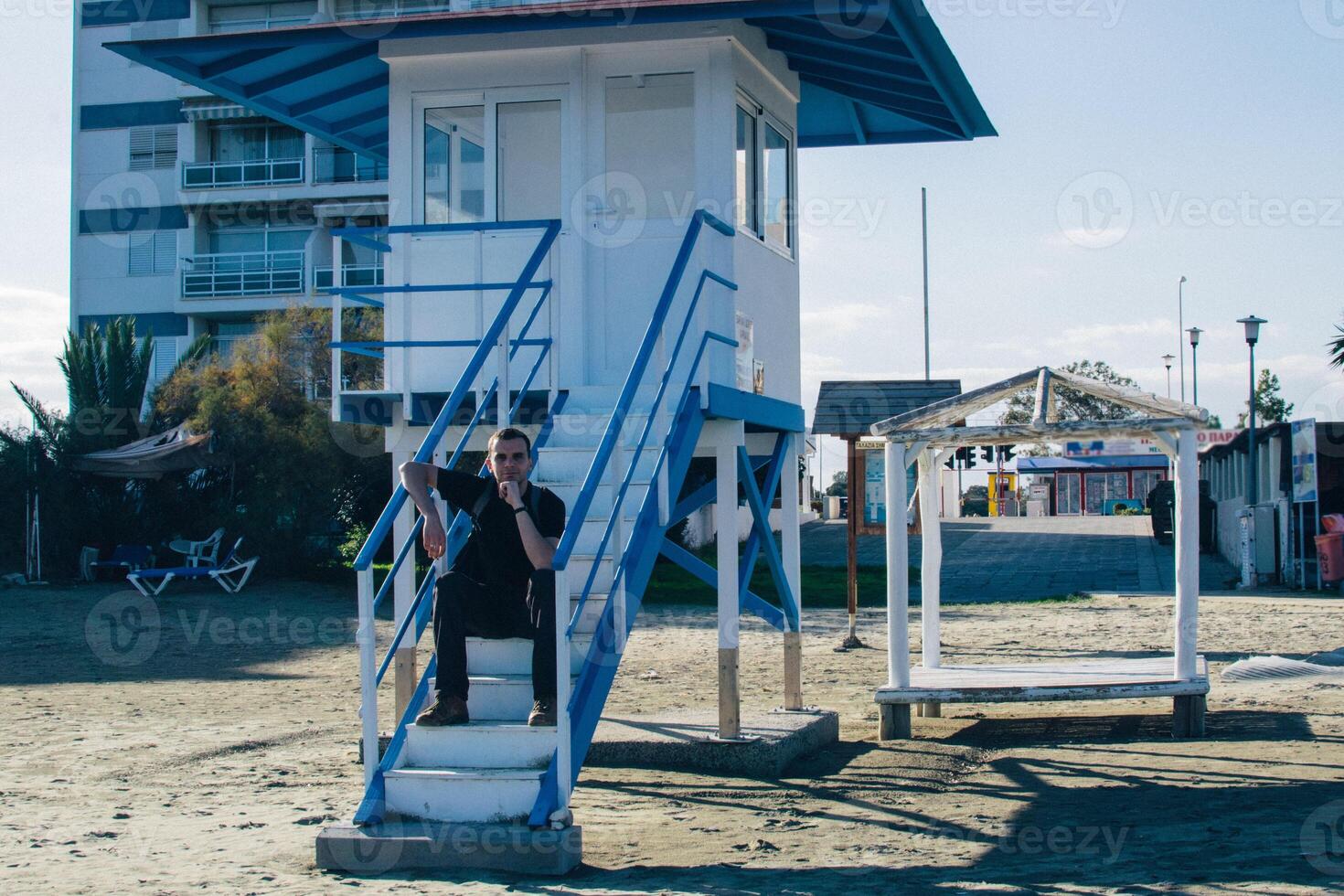 young man with a backpack sits on the steps of a lifeguard tower near the sea photo