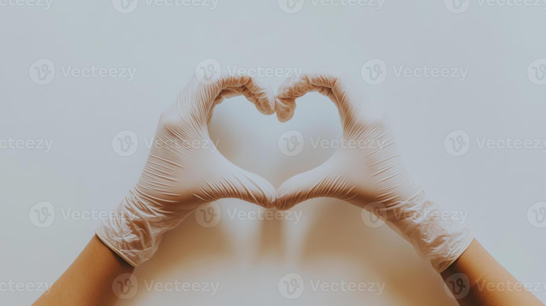 Hands forming heart shape with gloves against neutral background, healthcare and compassion concept photo