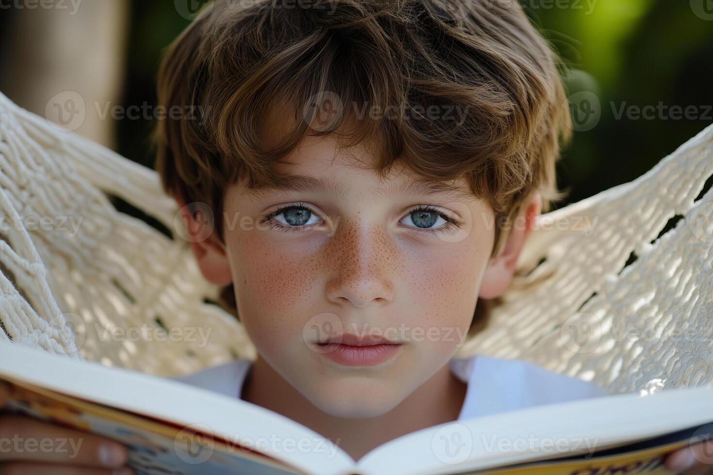 Young boy reading a book while relaxing in a hammock on a sunny day. photo